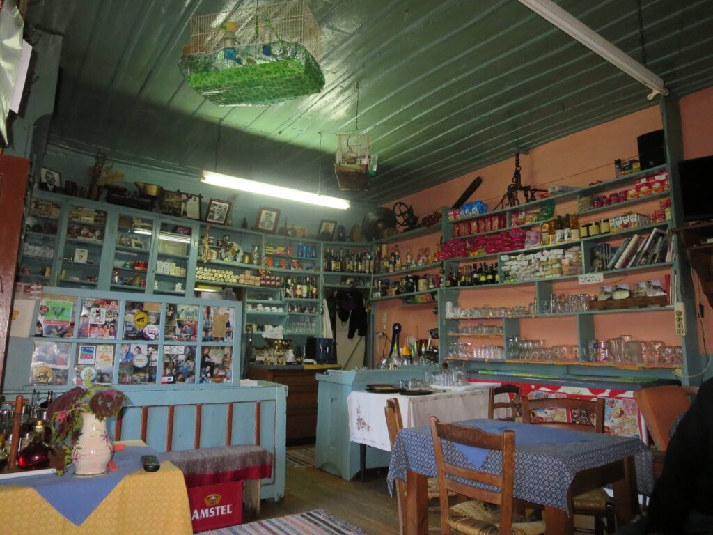 Kalarites magasi: cafe cum shop, with wide range of articles on shelves, bird in cage and simple tables