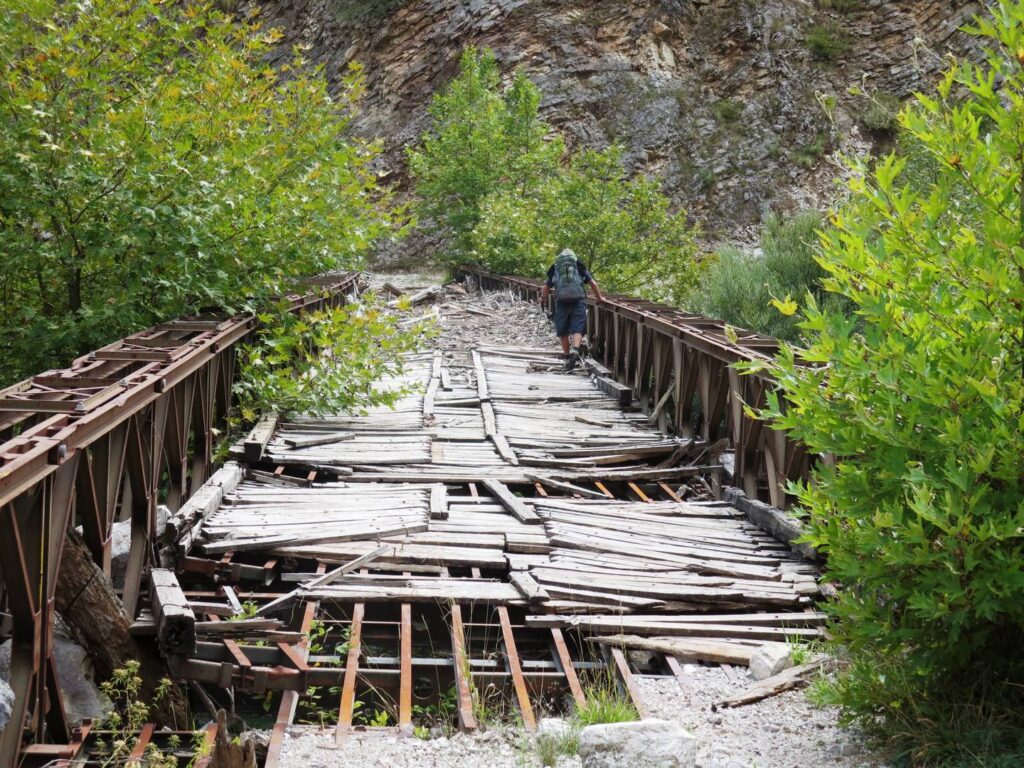 Hiker crossing the derelict Mesochora bridge with its surface destroyed in places