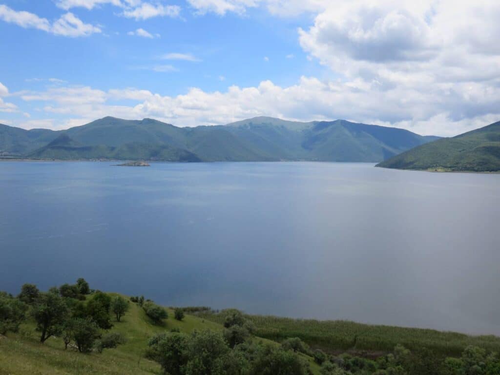 Still blue waters of Little Prespa Lake with mountains behind