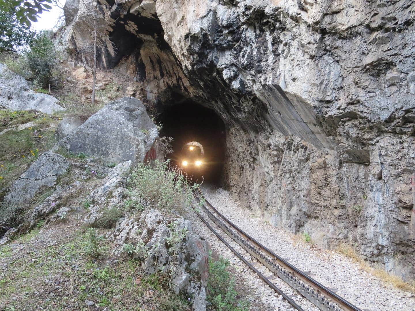Headlights of Kalavryta train coming out of narrow rocky tunnel on rack and pinion rails